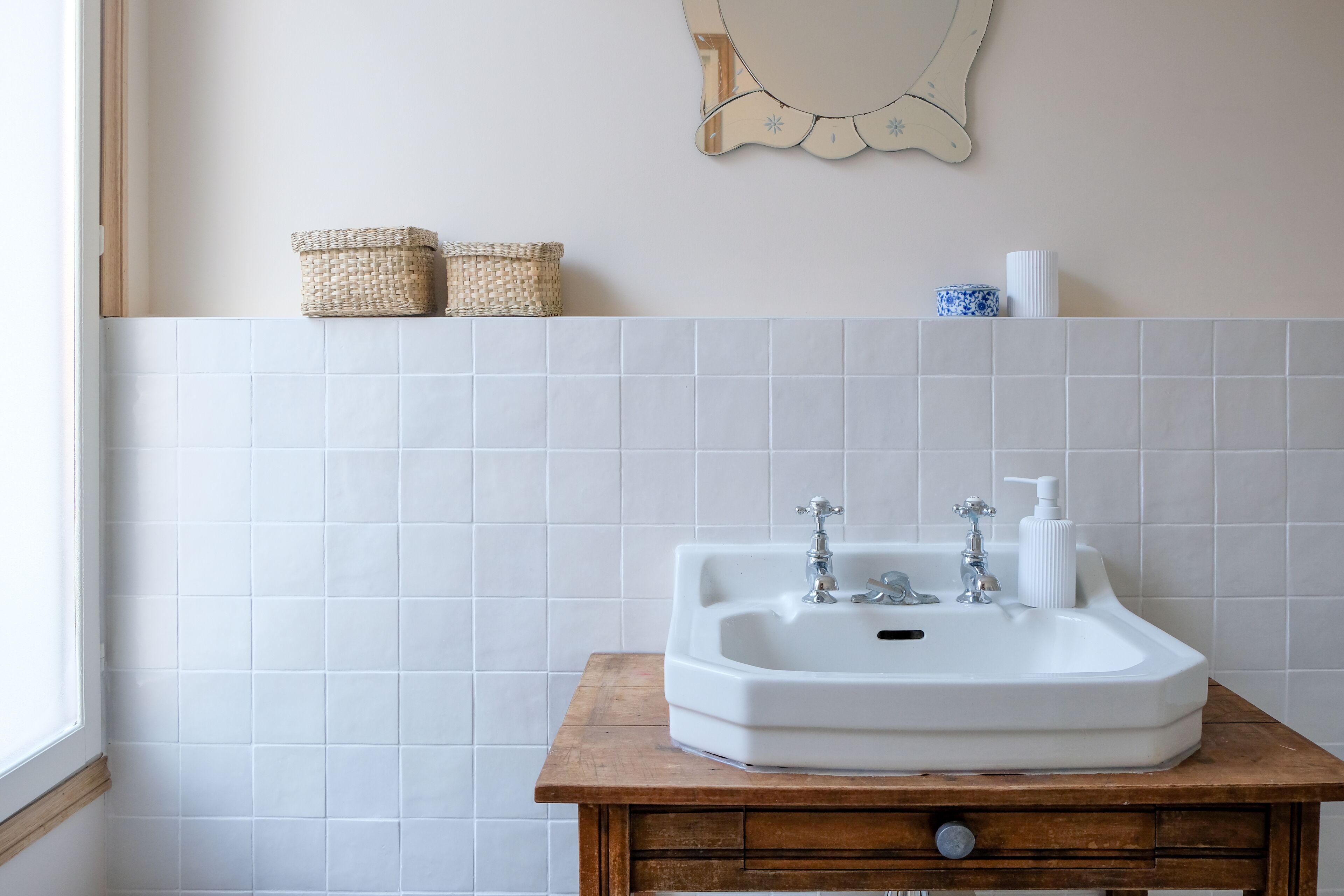 Un baño con lavamanos blanco, tocador de madera y paredes con azulejos.