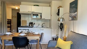A compact living space with a dining area, kitchenette, and a sofa with a yellow pillow. - Cozy Apartment in Montgenevre - Sleeps 4 (Montgenèvre)