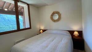A bedroom with a bed, a window, a wall-mounted mirror, and two bedside lamps. - Cozy Apartment in Montgenevre - Sleeps 4 (Montgenèvre)