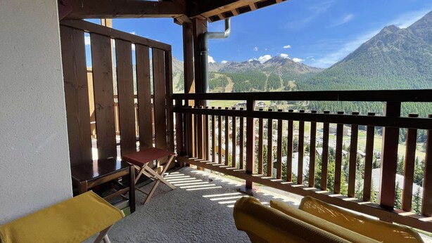 A balcony with a wooden railing, a folding chair, and a yellow bench. - Cozy Apartment in Montgenevre - Sleeps 4 (Montgenèvre)