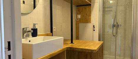 A modern bathroom with a wooden vanity, a large mirror, and a glass shower enclosure.