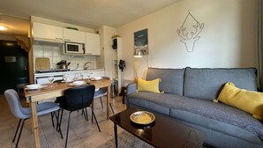 A compact living space with a dining area, kitchenette, and a sofa with cushions. - Cozy Apartment in Montgenevre - Sleeps 4 (Montgenèvre)