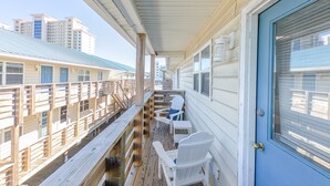 A covered balcony with wooden railings, a blue door, and two white Adirondack chairs. - 2BR Beach Getaway w/ Pool walkable to The Hangout!  ~ Walk to beach in 3 minutes (Gulf Shores)
