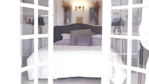 Quarto com cama, mesas de cabeceira, luminária na parede e uma janela.