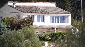 Uma casa de dois andares com telhado ladrilhado, paredes brancas e várias janelas.