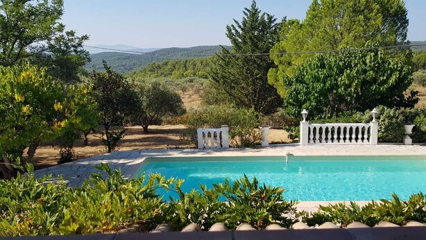 Piscina com vista para uma paisagem montanhosa, rodeada por vegetação e um muro branco.