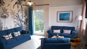 Sala de estar com dois sofás azuis, uma mesa de centro e uma parede com um mural tropical.