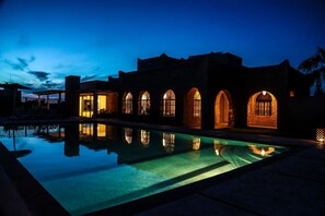 A poolside view of a building with arched windows and stone walls at dusk.