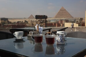 A table with two cups and a teapot, set against a backdrop of pyramids and a desert landscape.