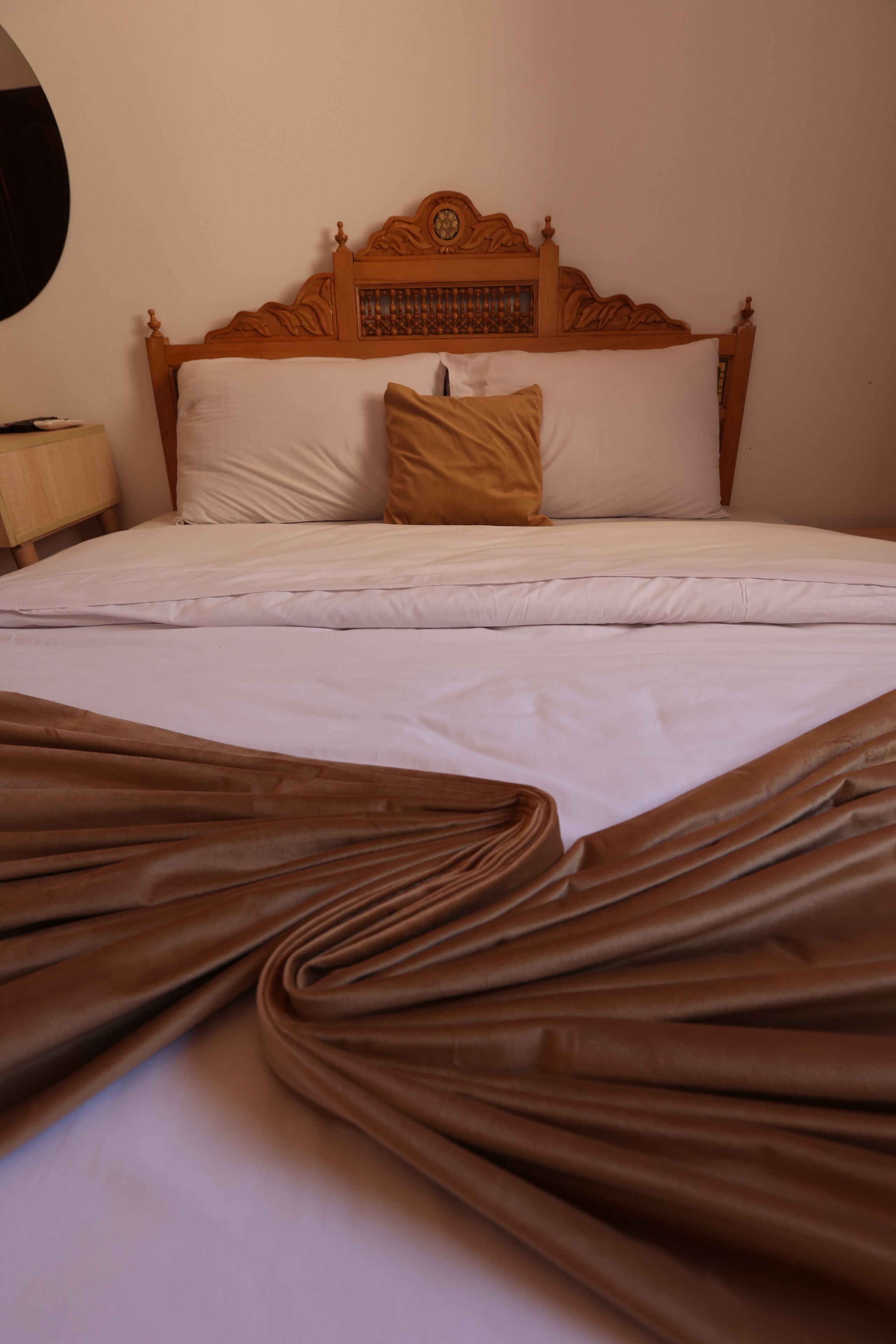 Una cama bien hecha con cabecera de madera, ropa de cama blanca y una manta marrón.