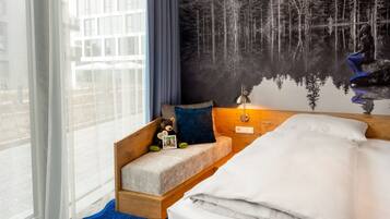 A bedroom with a bed, a nightstand, a lamp, a teddy bear, and a mural of a forest.