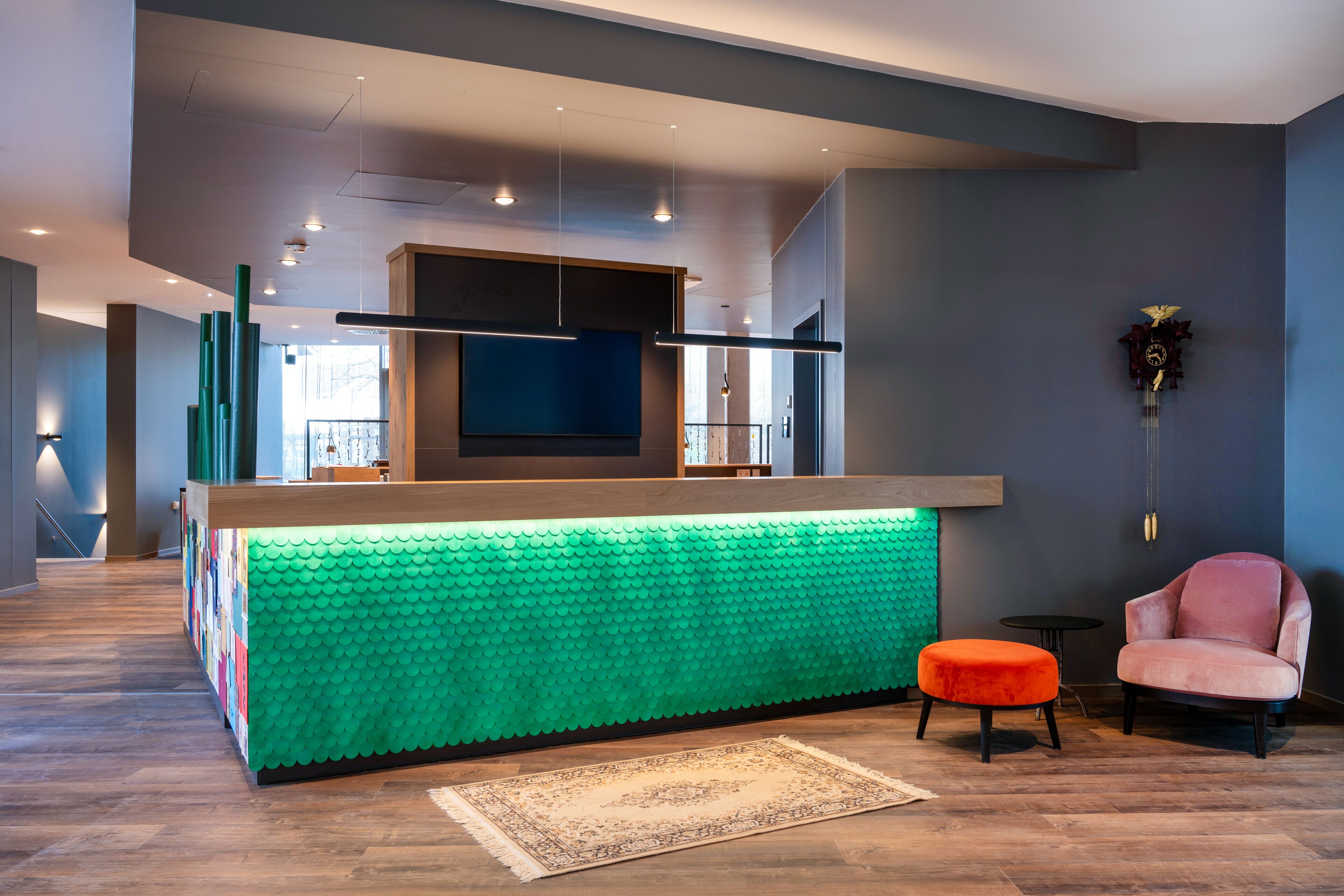 A modern living room with a green textured coffee table, a pink armchair, and a flat-screen TV mounted on the wall.