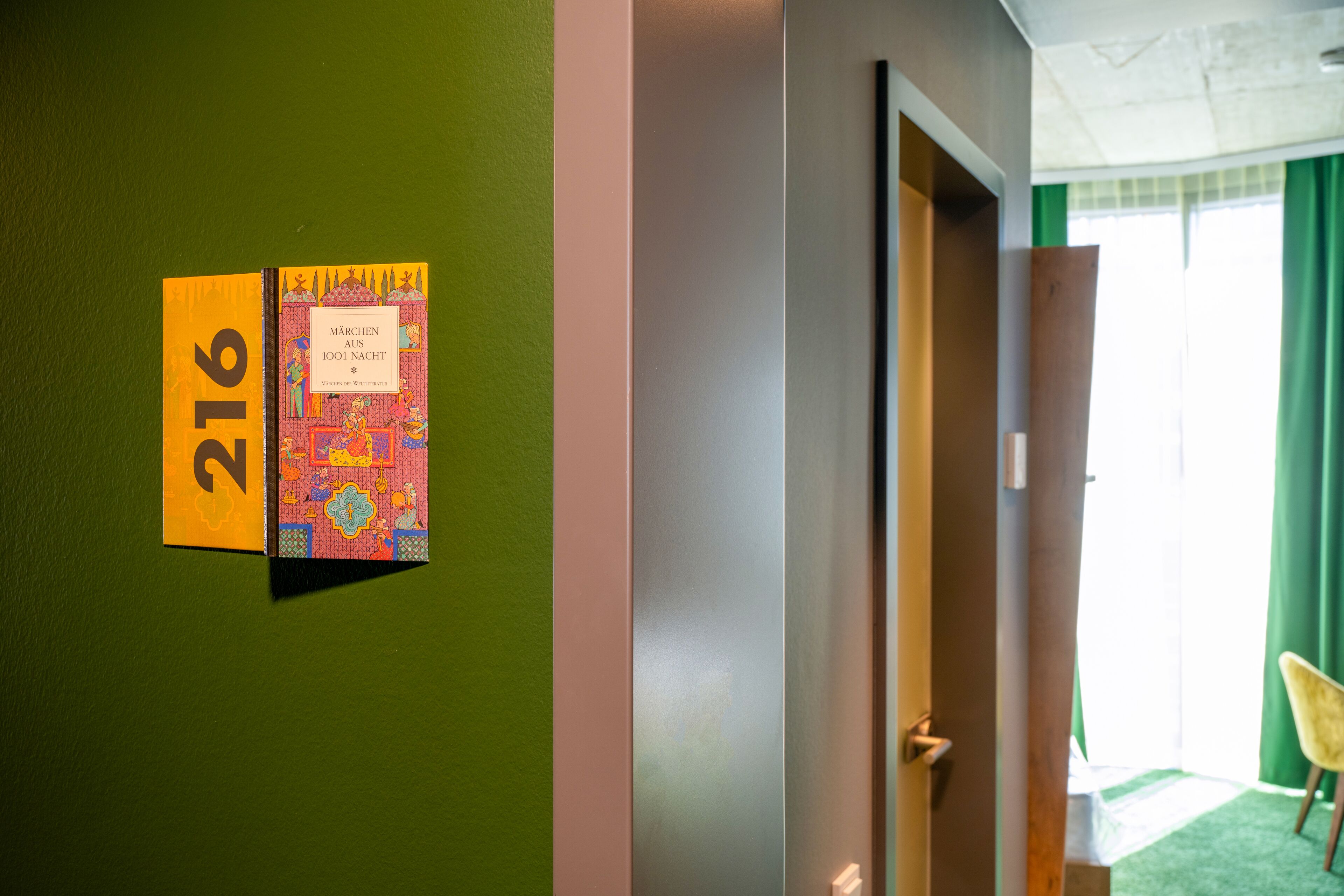 A hotel room with a green wall, a door, and a window with green curtains.