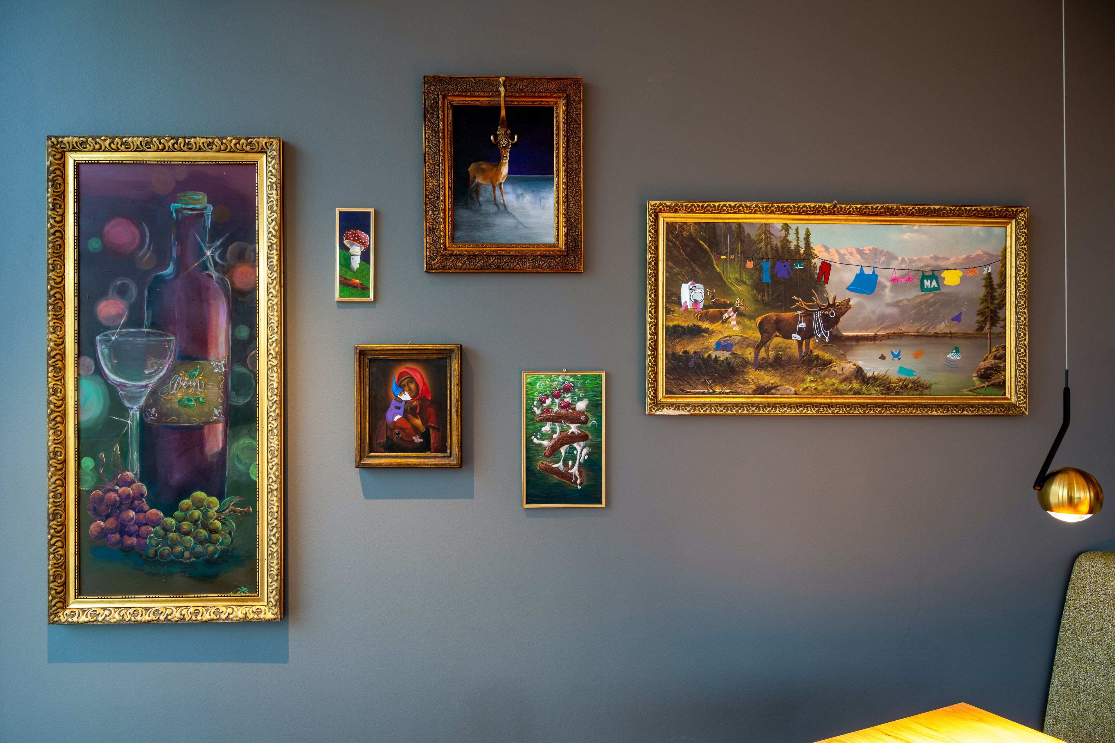 A wall with various framed artworks, including a painting of a deer, a landscape, and still life.