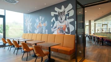 Un restaurante moderno con asientos anaranjados, mesas de madera y un mural en la pared.