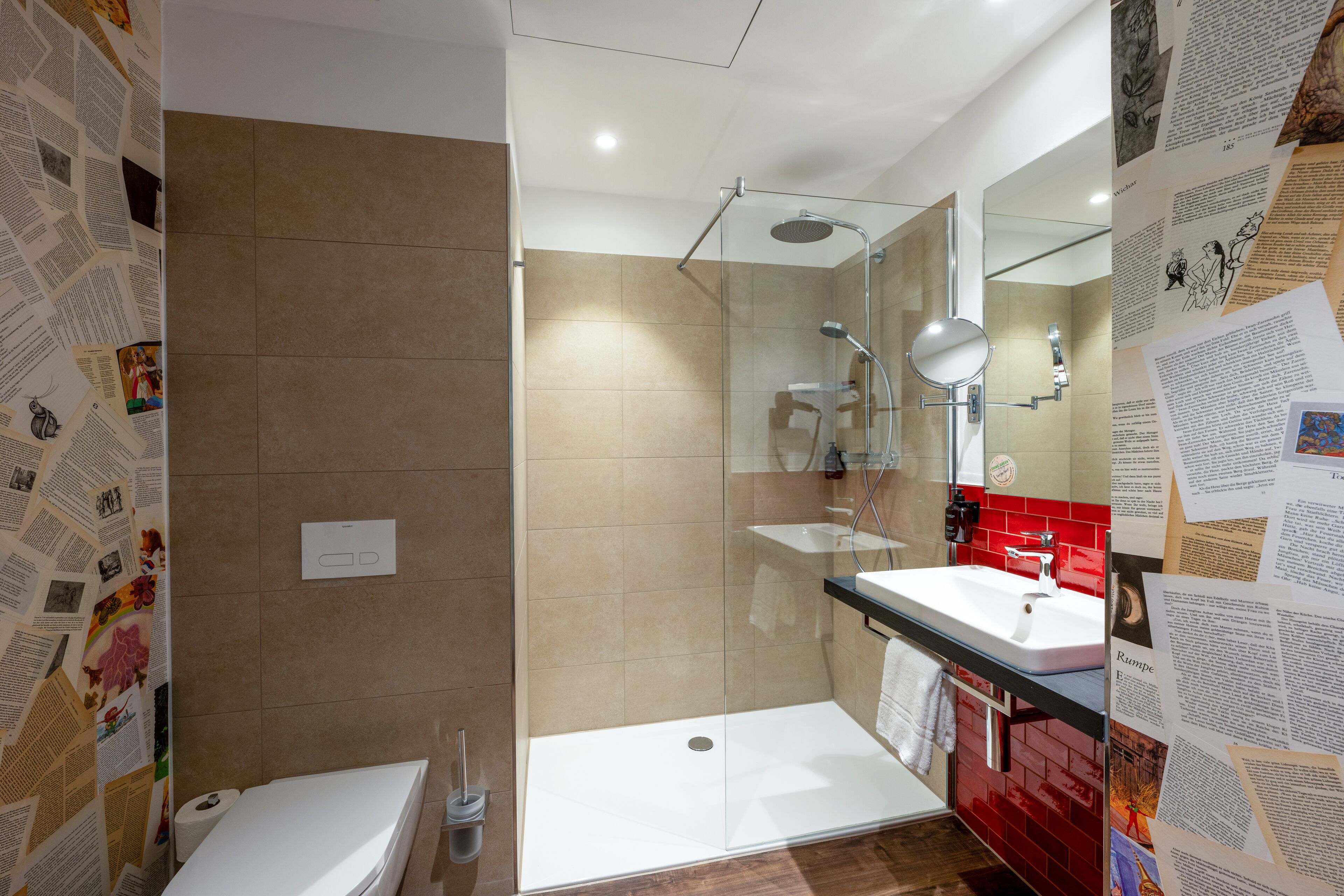 Un baño moderno con ducha envuelta en vidrio, un lavabo blanco y un pared con azulejos rojos.