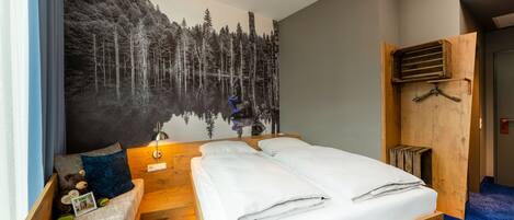 A hotel room with a bed, a wooden bench, a wall mural, and a wooden wardrobe.