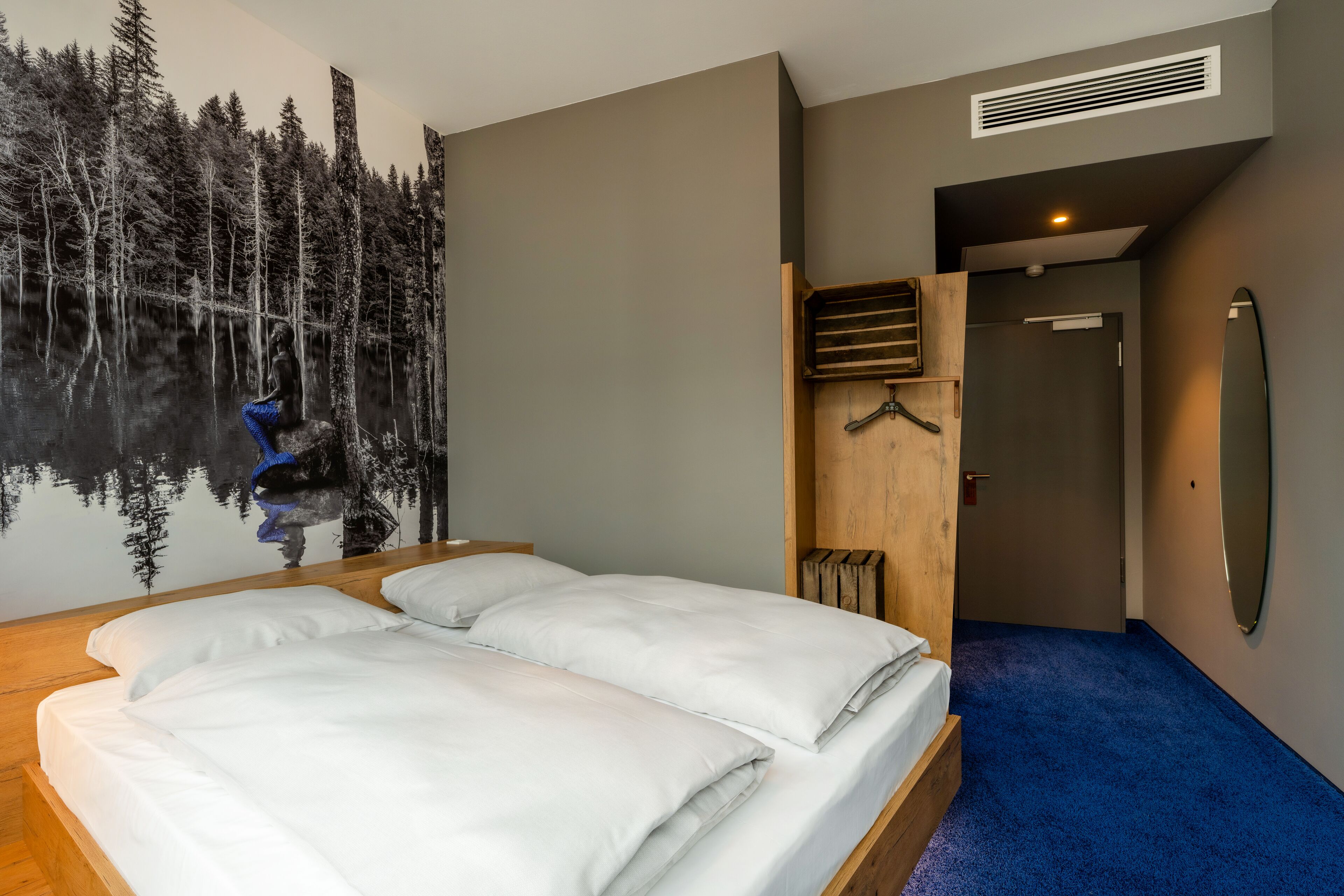 Un dormitorio con cama, un mural en la pared, un banco de madera y una puerta que da a otra habitación.