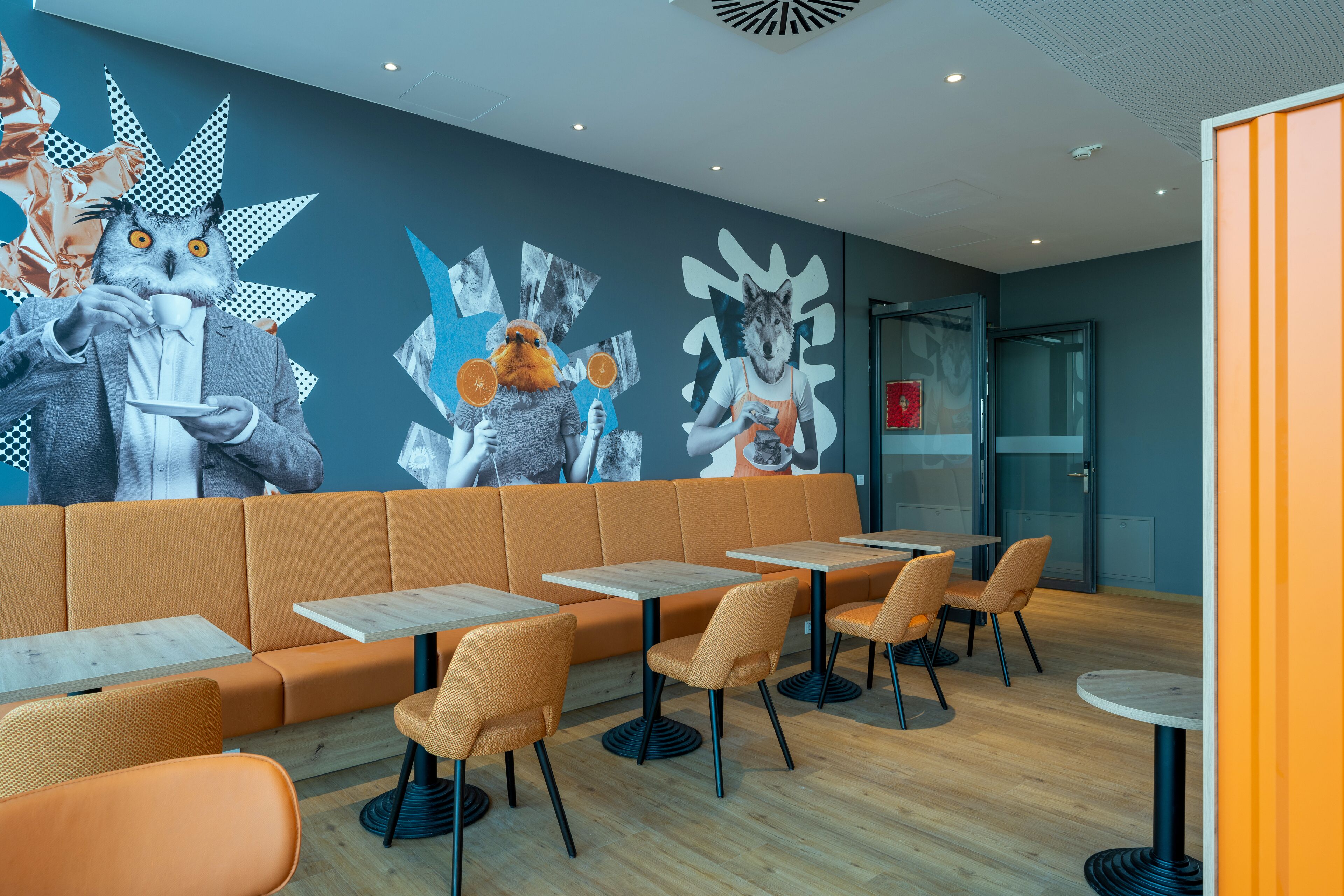 A modern restaurant with orange seating, wooden tables, and a mural of animal heads on the wall.