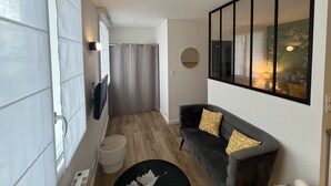 A modern living room with a dark grey sofa, a round mirror, and a large window with a view of a building. - Studio Osaka - Hyper Centre Lorient (Lorient)
