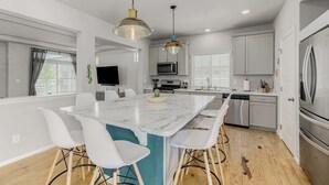A modern kitchen with white cabinets, a central island with bar stools, and stainless steel appliances. - Monthly Stays! Denver Chile House (Commerce City)