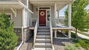 A two-story house with a front porch, a red door, and a small garden area. - Monthly Stays! Denver Chile House (Commerce City)