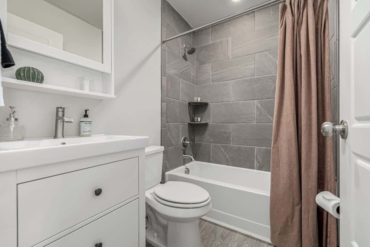 A bathroom with a white vanity, a toilet, a bathtub, and a shower area.