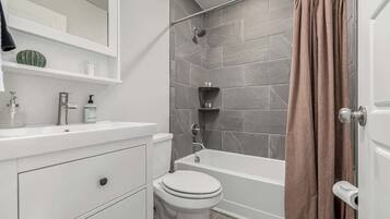 A bathroom with a white vanity, a toilet, a bathtub, and a shower area.