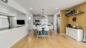 A modern kitchen with white cabinets, a central island with chairs, and a hanging light fixture. - Monthly Stays! Denver Chile House (Commerce City)
