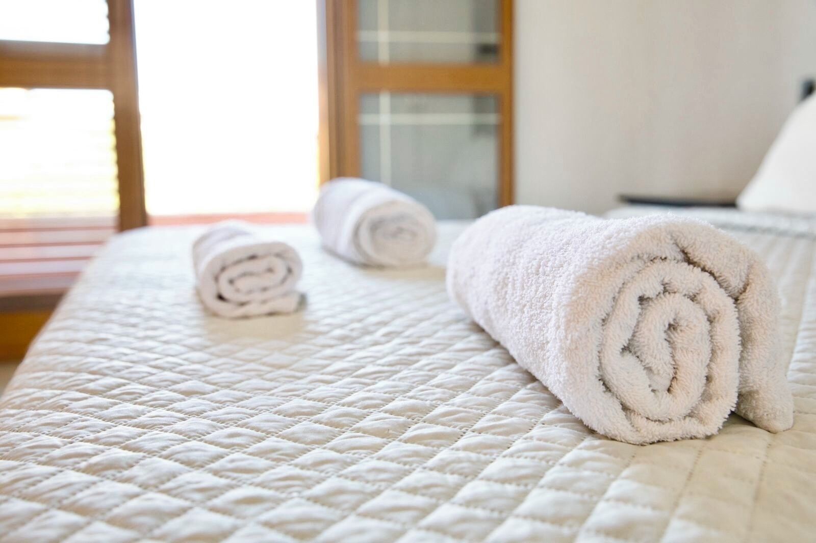A neatly made bed with a quilted white bedspread and two rolled white towels.