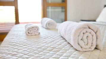 A neatly made bed with a quilted white bedspread and two rolled white towels.