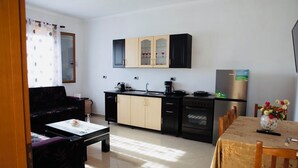 Een kleine keuken met een zithoek, met een bank, een tafel met een bloevas en een koelkast.