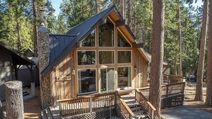 Une cabane dotée d’une cheminée en pierre, de grandes fenêtres et d’une terrasse en bois.