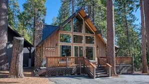 Une cabane en rondins dotée d’une grande façade vitrée, d’une terrasse en bois et d’une cheminée en pierre.