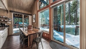Une cuisine spacieuse avec une grande table à manger et des chaises, des armoires en bois et une vue sur une terrasse extérieure enneigée.