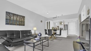 Een moderne woonkamer met een zwarte leren bank, een glazen salontafel en een eethoek met een witte tafel en stoelen.
