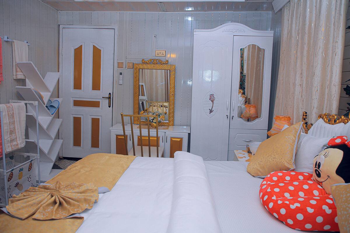 Une chambre d’hôtel comprenant un lit, une coiffeuse avec un miroir, une commode et un jouet en peluche à l’effigie de Mickey Mouse.