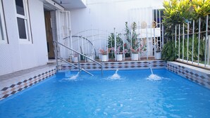 A swimming pool with a tiled border, a metal ladder, and potted plants around the pool area. - AFRIKANDO ROYAL CASTLE (Dar es Salaam)