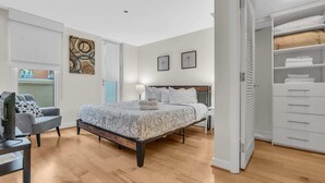Une chambre à coucher avec un lit, un bureau, une chaise, une armoire et un tableau accroché au mur.