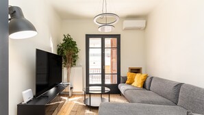 Ein modernes Wohnzimmer mit einem Flachbildfernseher, einem grauen Sofa, einem kleinen runden Tisch und einer großen Topfpflanze.