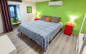 Une chambre à coucher avec un lit, deux tables de chevet avec des lampes, une plante en pot, une fenêtre avec des rideaux et une petite table.