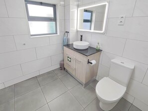 Une salle de bain moderne équipée de toilettes, d’un lavabo, d’un miroir et d’une fenêtre.