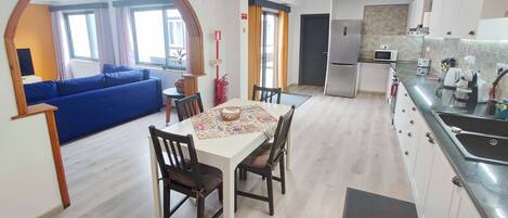 A modern kitchen with a dining area, a blue sofa, and a visible fire extinguisher.