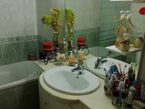 Un baño con lavabo, dos espejos, bañera y distintos artículos de aseo.