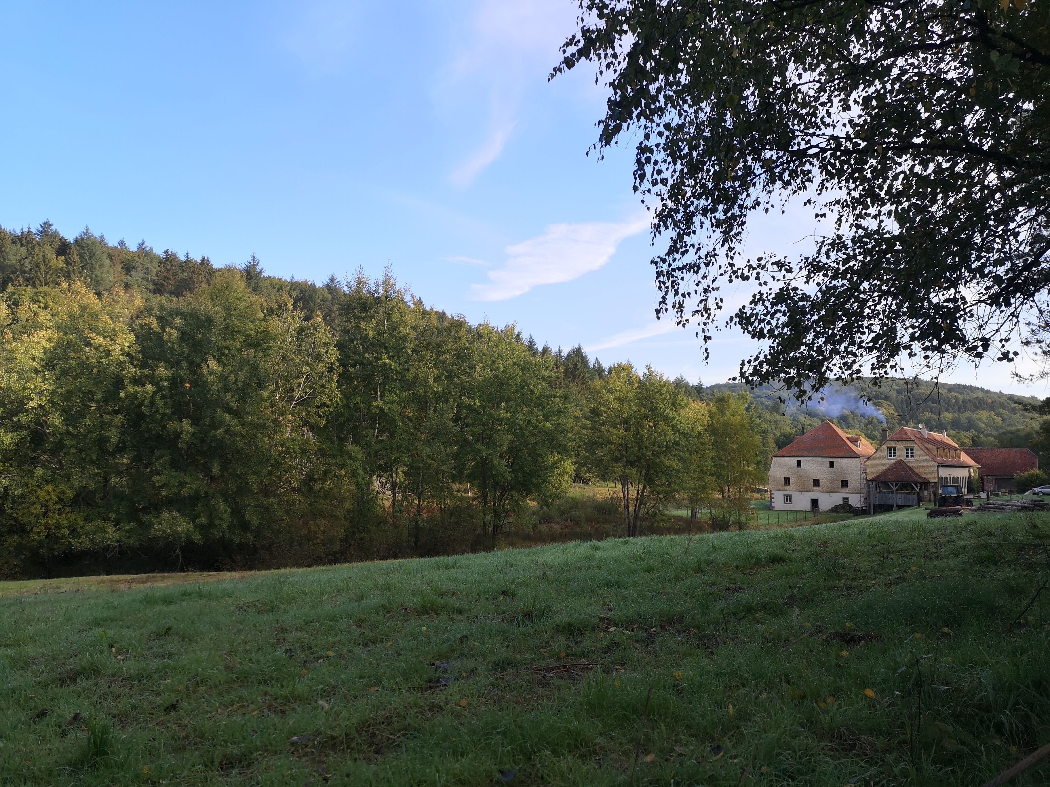 A rural landscape with a traditional stone building, surrounded by lush greenery and a clear sky.