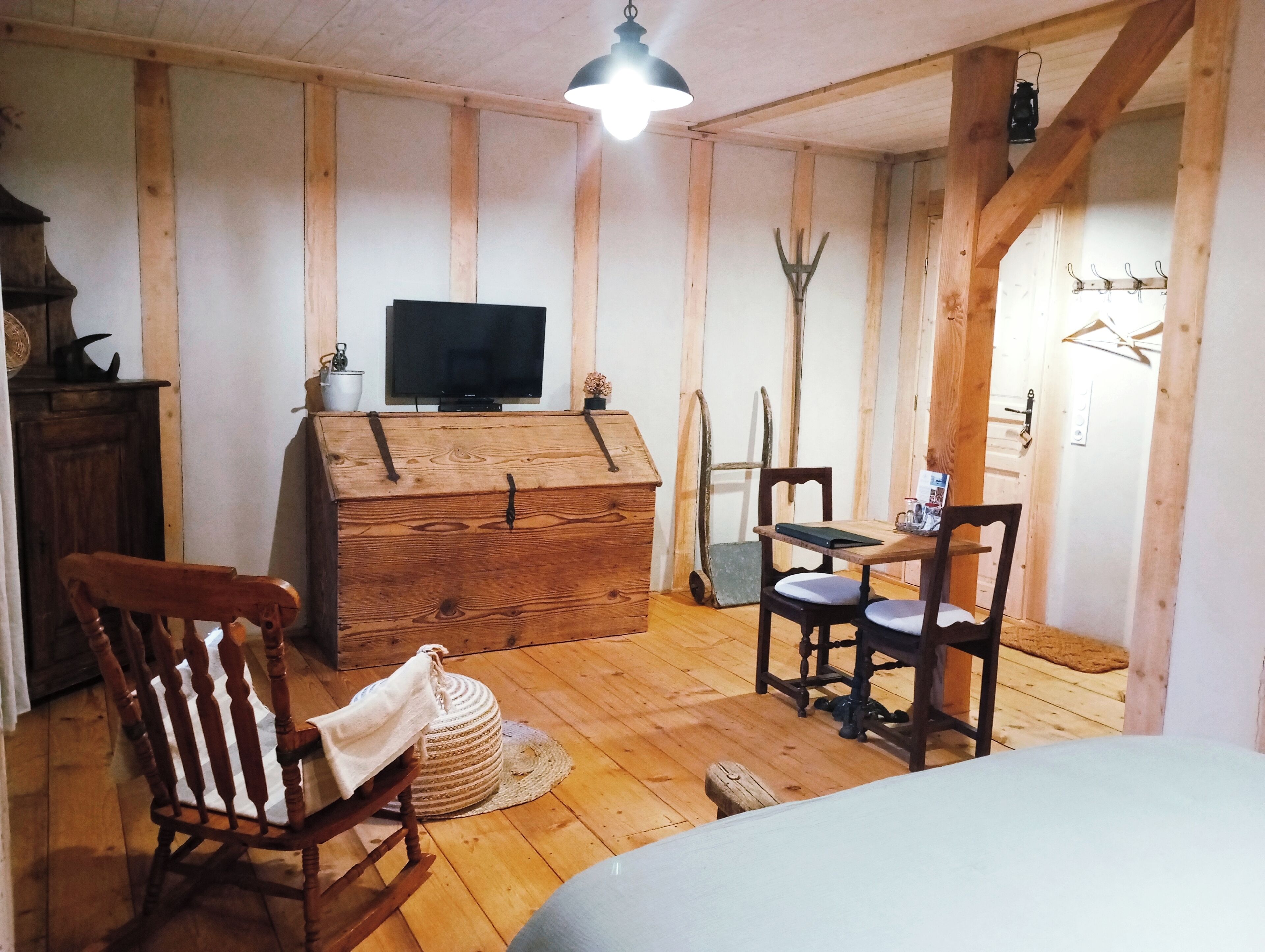 A cozy room with wooden walls, a wooden chest, a television, a rocking chair, and a dining table with chairs.