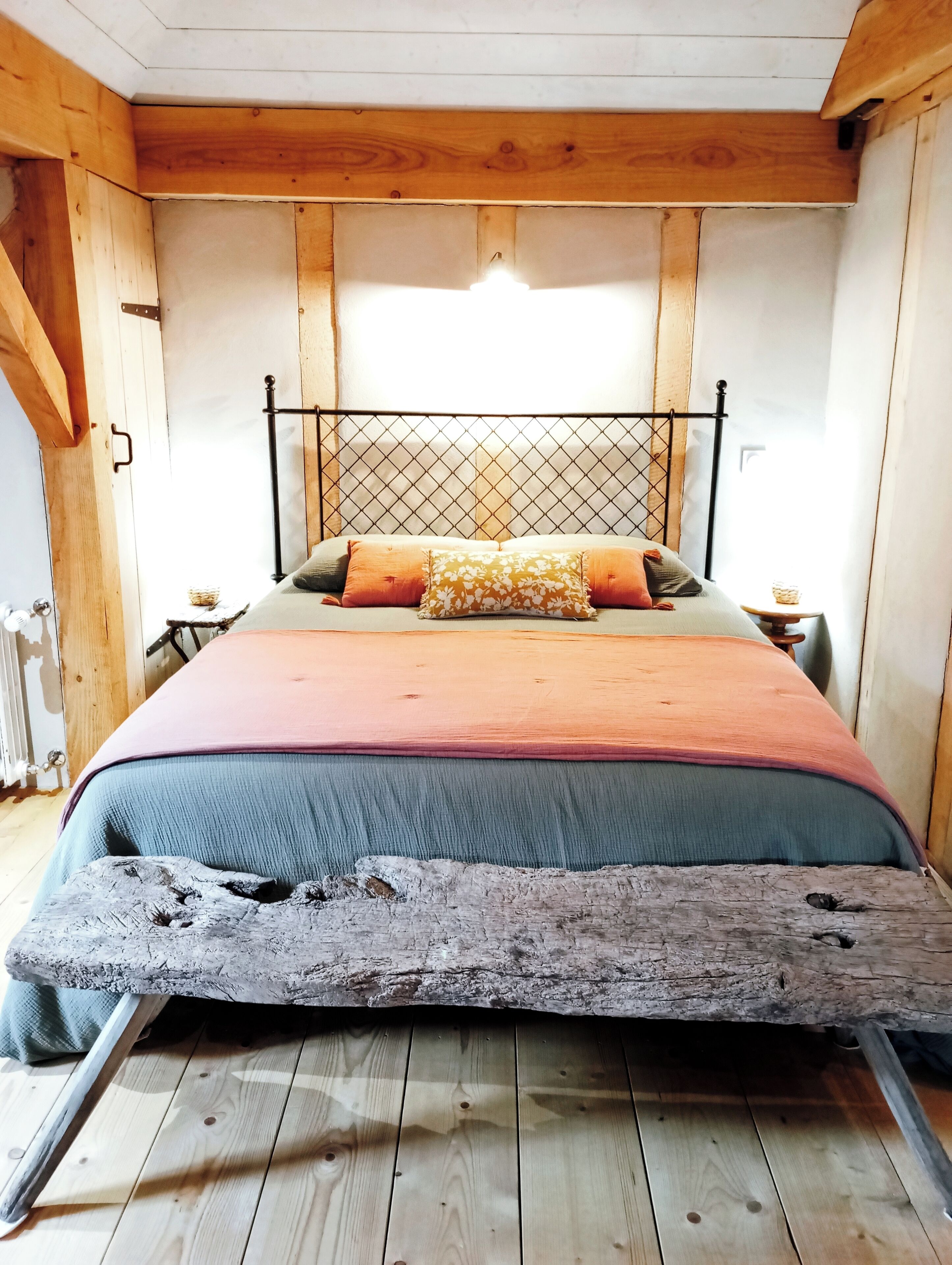 Ein Bett mit Metall-Kopfstück, Holzwänden und rustikalem Boden.