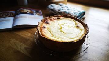 Une tarte posée sur une grille de refroidissement en métal, sur une table en bois, avec un livre et un tissu en arrière-plan.