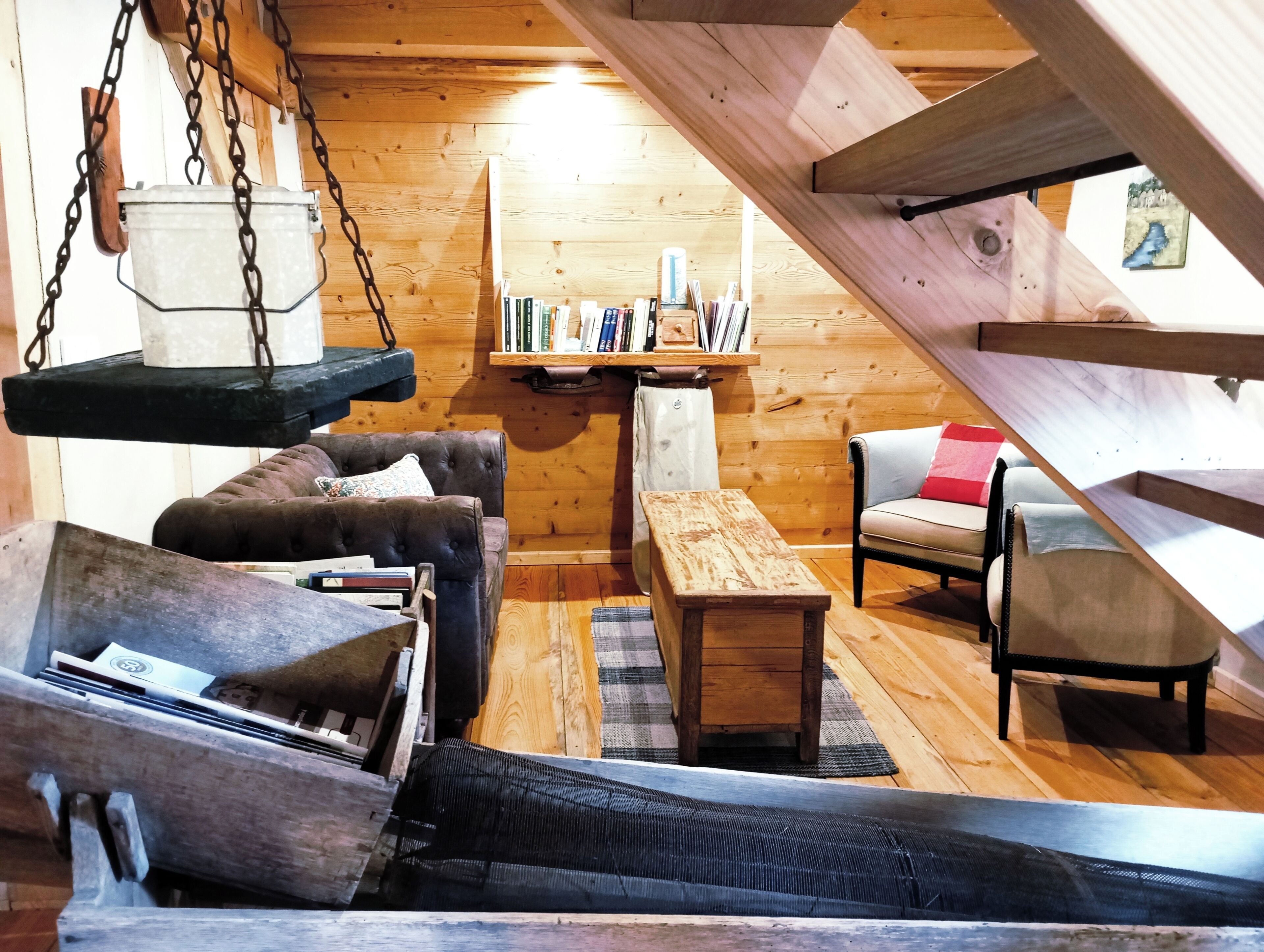 A cozy cabin interior with a loft bed, a cushioned chair, a wooden bench, and a bookshelf.