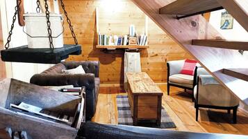 A cozy cabin interior with a loft bed, a cushioned chair, a wooden bench, and a bookshelf.